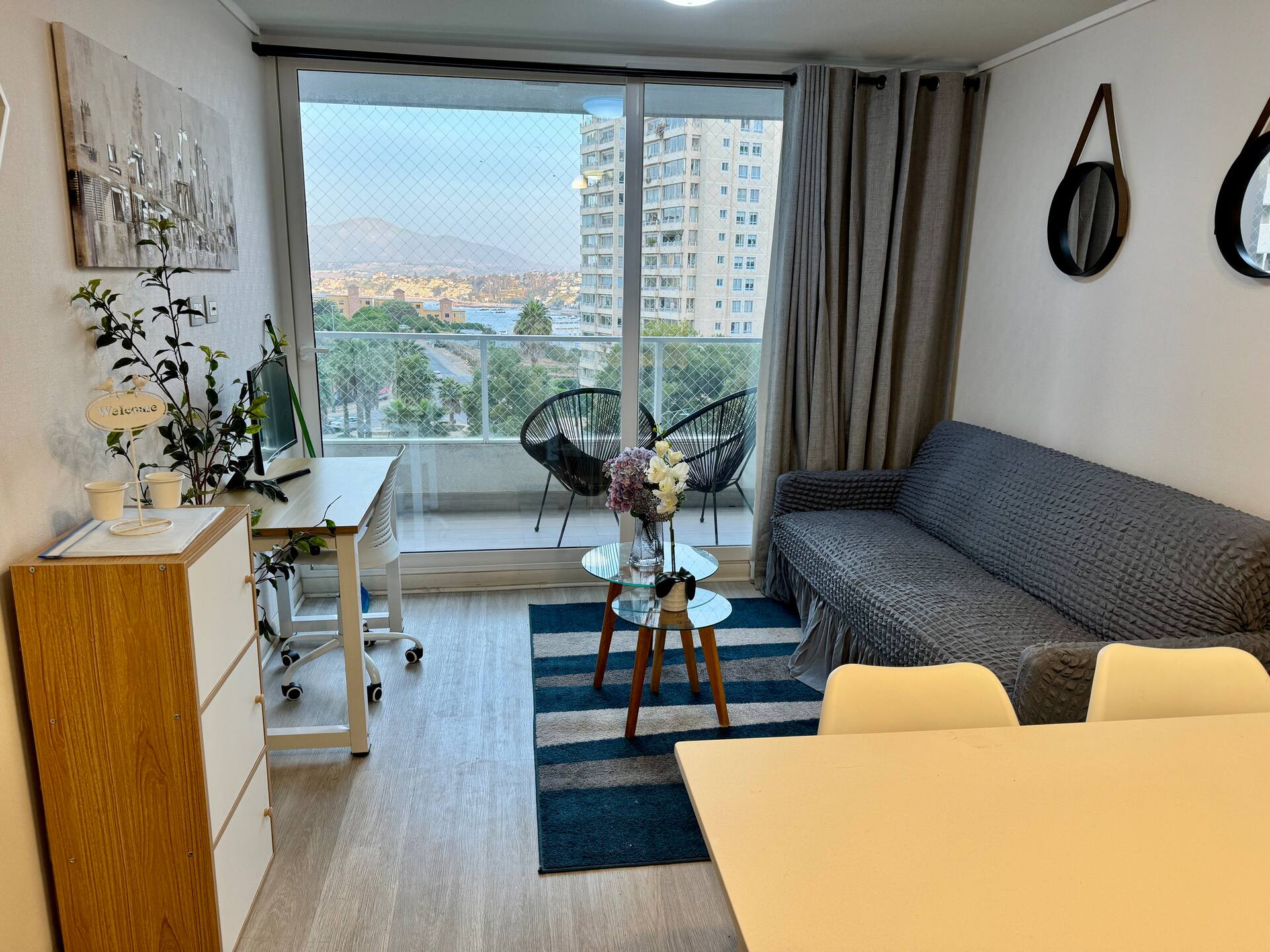 Living del departamento con vista al mar de Valparaíso, sofá gris, balcón con sillas acapulco